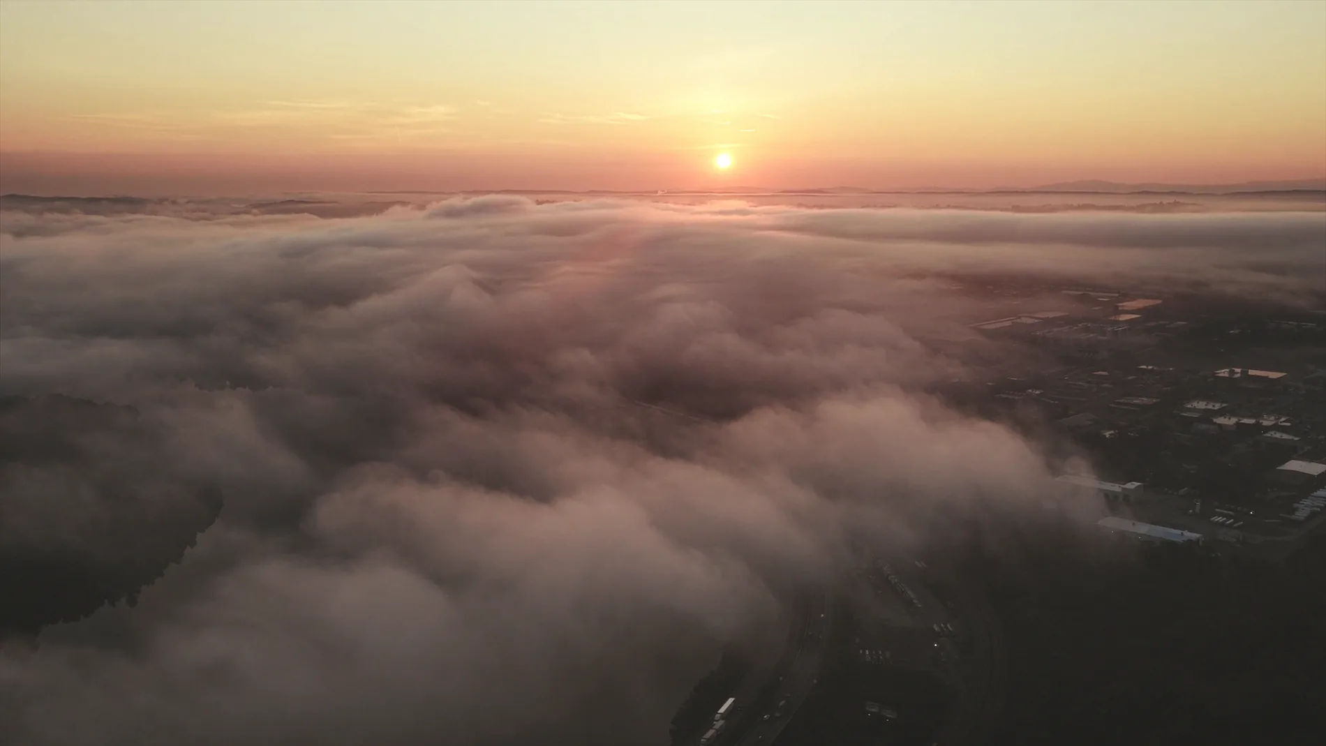 Sunrise over a sea of fog with a Melbourne industrial estate emerging on the far side — the light of Chapter I, now risen